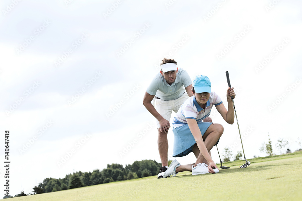 Mid-adult man looking at woman aiming ball on golf course