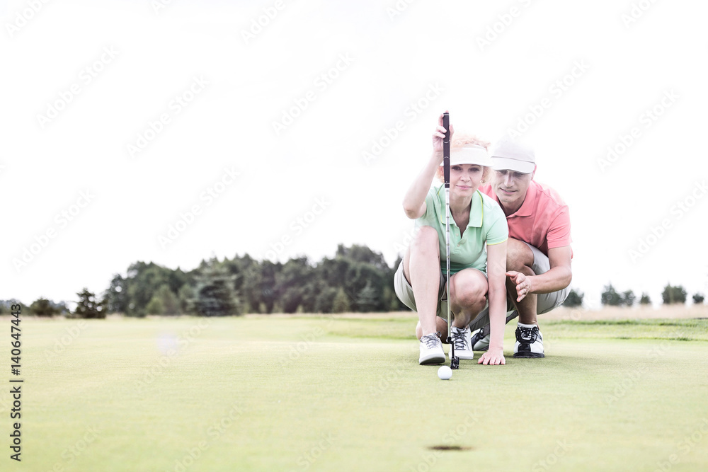 Obraz premium Man assisting woman aiming ball on golf course against clear sky