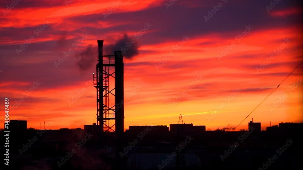 Industrial pipe with smoke in the city on the background of the red dawn.