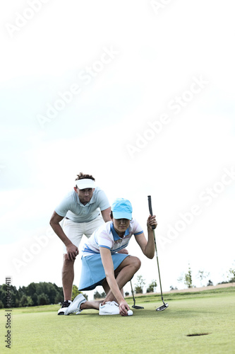 Man looking at woman aiming ball on golf course against sky