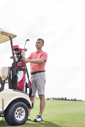 Middle-aged man standing by cart at golf course