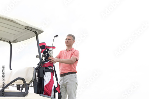 Thoughtful middle-aged man standing by cart against clear sky