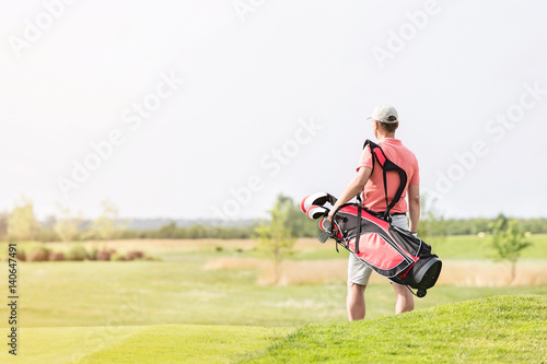 Rear view of man carrying golf club bag while walking at course