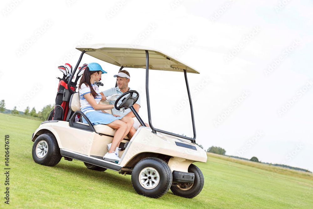 Couple looking at each other while sitting in golf cart against clear sky Couple looking at each other while sitting in golf cart against clear sky