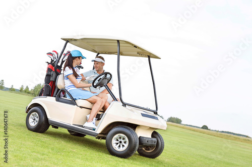 Couple looking at each other while sitting in golf cart against clear sky