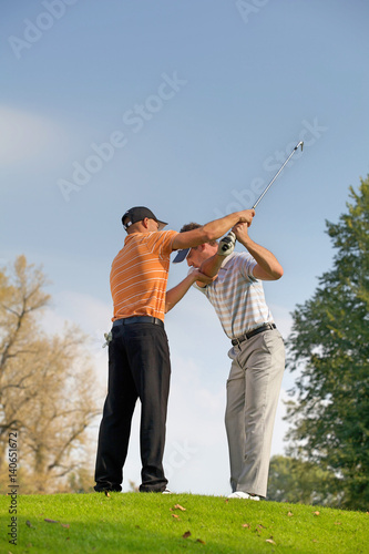 Golf professional helping young man with his swing