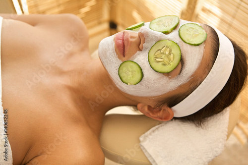 Young woman lying down on massage table with cucumbers on eyes and face