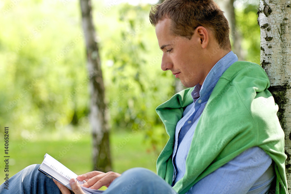 Fototapeta premium Young man reading book in park