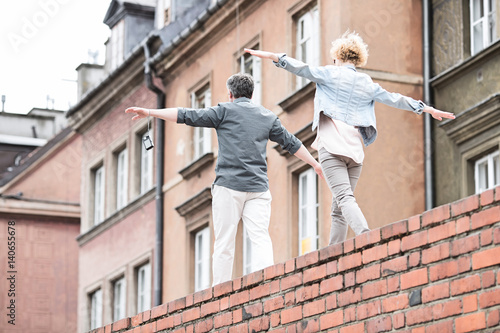Rear view of middle-aged couple with arms outstretched walking on brick wall © moodboard