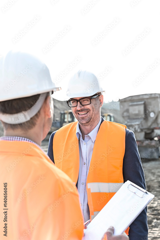 Happy engineers discussing at construction site against clear sky Happy engineers discussing at construction site against clear sky