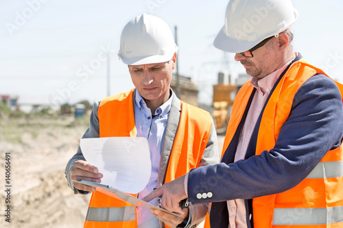 Engineers examining documents on clipboard at construction site against clear sky