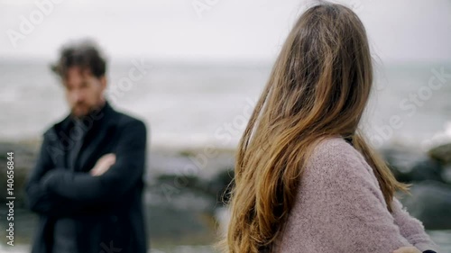 Sad woman looking angry boyfriend after fight standing in front of the ocean