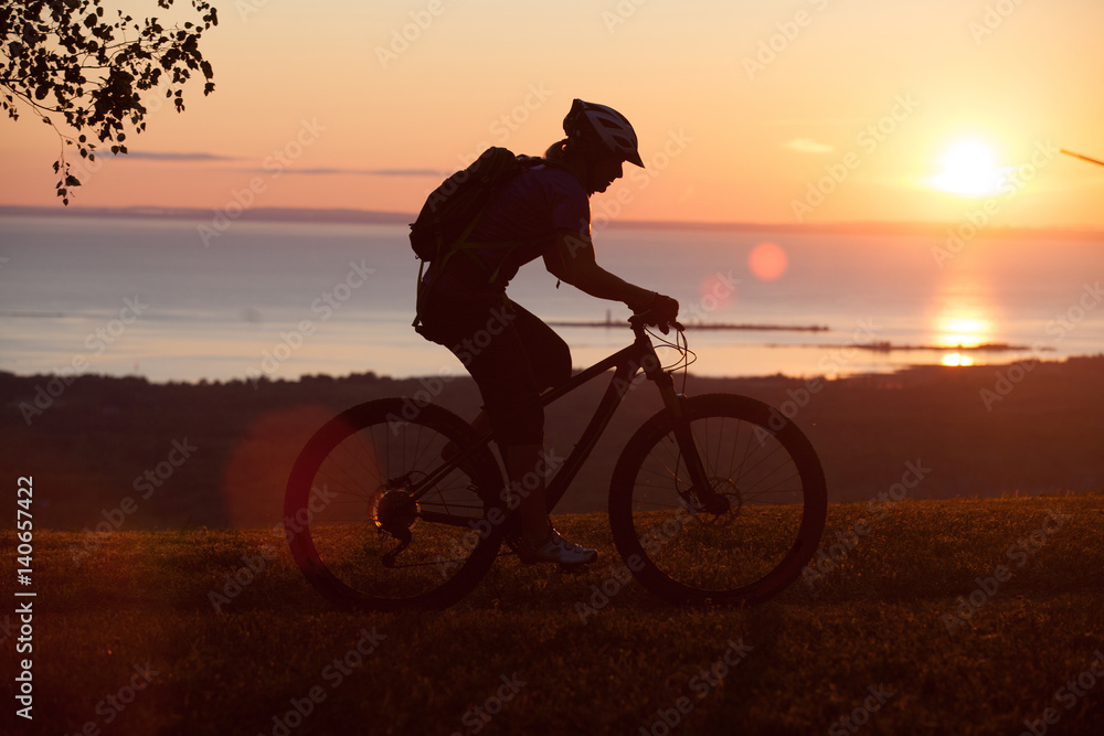 Fototapeta premium Woman mountain biking on single track trail at Sunset