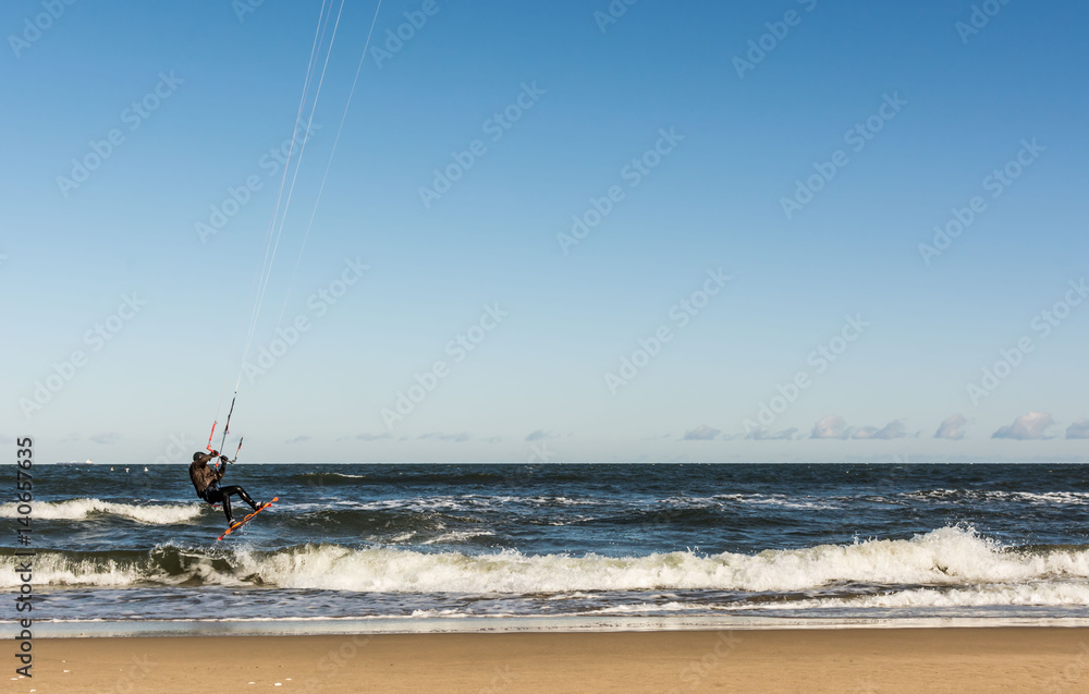 Kiteboarder in winter clothes flying over waves against blue sky in strormy winter's day, on the beach near Gdansk, Poland.