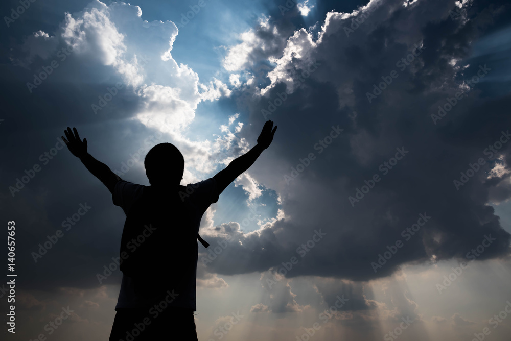 Silhouette of man with hands raised and sky with sunlight