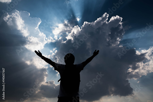 Silhouette of man with hands raised and sky with sunlight