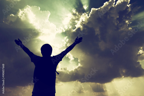 Silhouette of man with hands raised and sky with sunlight © stcom