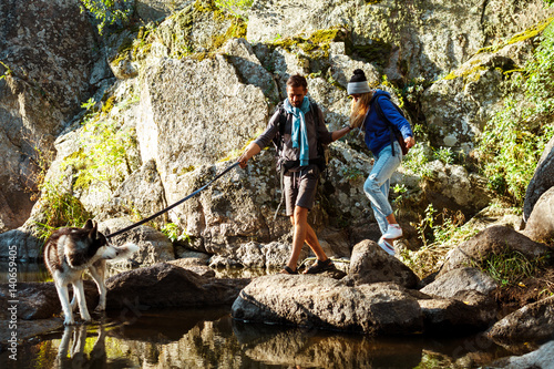 Young couple walking with huskies dog in canyon near water.