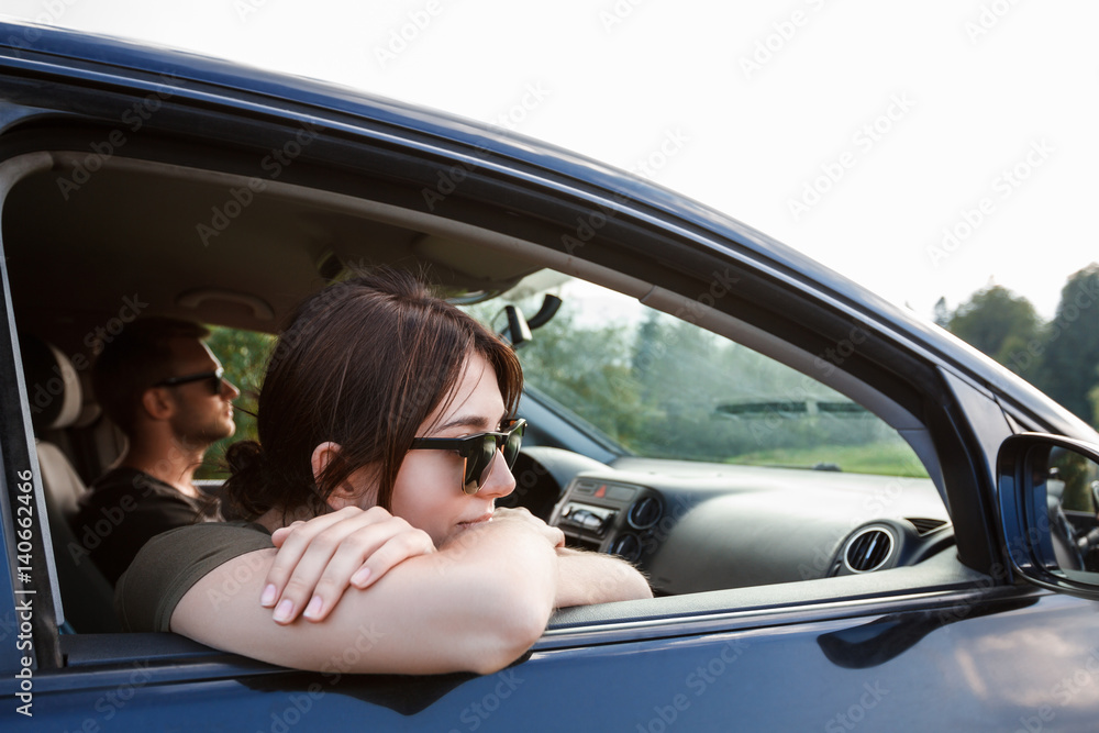 Young couple smiling, sitting in car, enjoying mountains view.