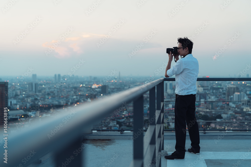 Asian man taking photo on building rooftop in low light situation. Photography, office people, or hobby concept. With copy space