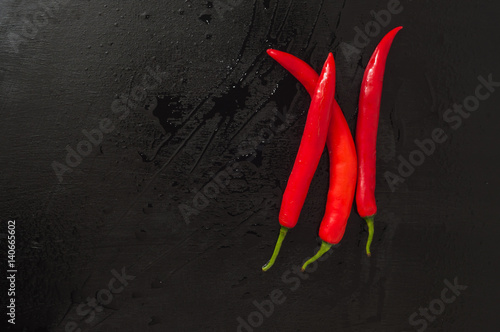 Three fresh red chili peppers on dark kitchen surface with water drops