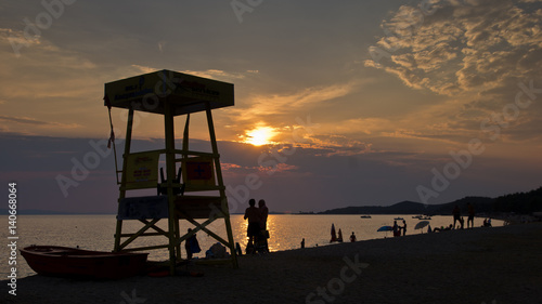 Silhouette of a lifegueard watchtower, boat and people on a beach at sunset, Sithonia, Greece