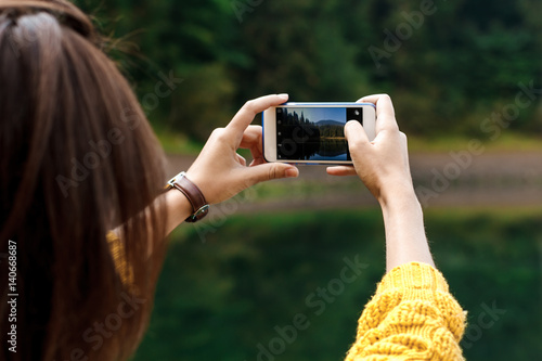 Pretty brunette girl taking photo of beautiful mountains view.