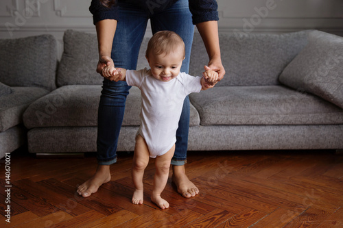 baby learning to walk on a wood floor with his mother holding his hands