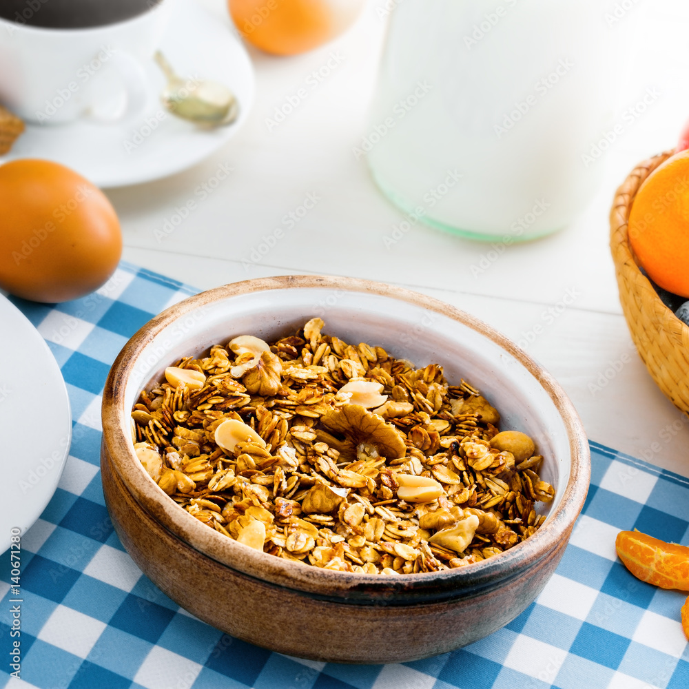 Breakfast made of oatmeal granola, croissants, milk, eggs, coffee and fruits on a table. Delicious healthy food.