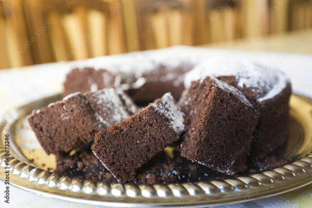 Homemade chocolate cake, with sugar glass on top, on a golden tray. Horizontal shot with natural light from a window.