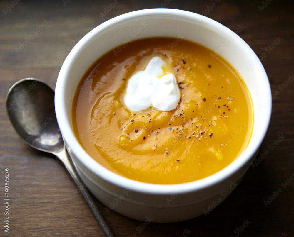Butternut squash soup in a bowl with a spoon and sour cream garnish. Butternut squash soup in a bowl with a spoon and sour cream garnish.