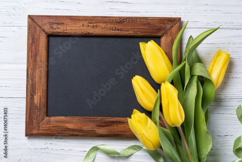 Chalkboard and yellow tulips bouquet on wooden background, top view with copy space