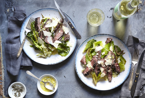 Steak and romaine on two plates with white wine.