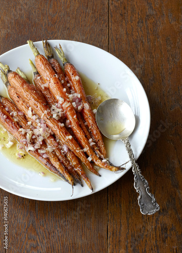 Roasted carrots on a plate with shallot and oil garnish.