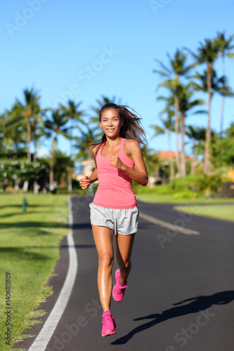 Healthy Asian woman runner jogging on urban road. Fitness girl athlete working out living an active lifestyle training cardio in the morning running in pink activewear. Full body.