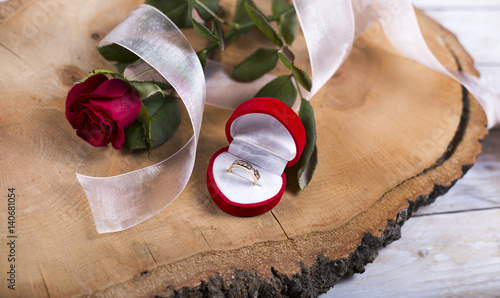 Marriage proposal with gold ring and red rose on wooden photo