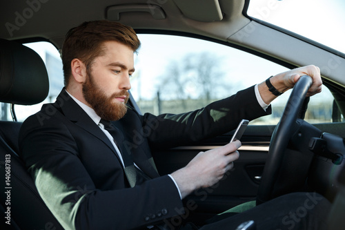 Side view of serious business man using phone at wheel