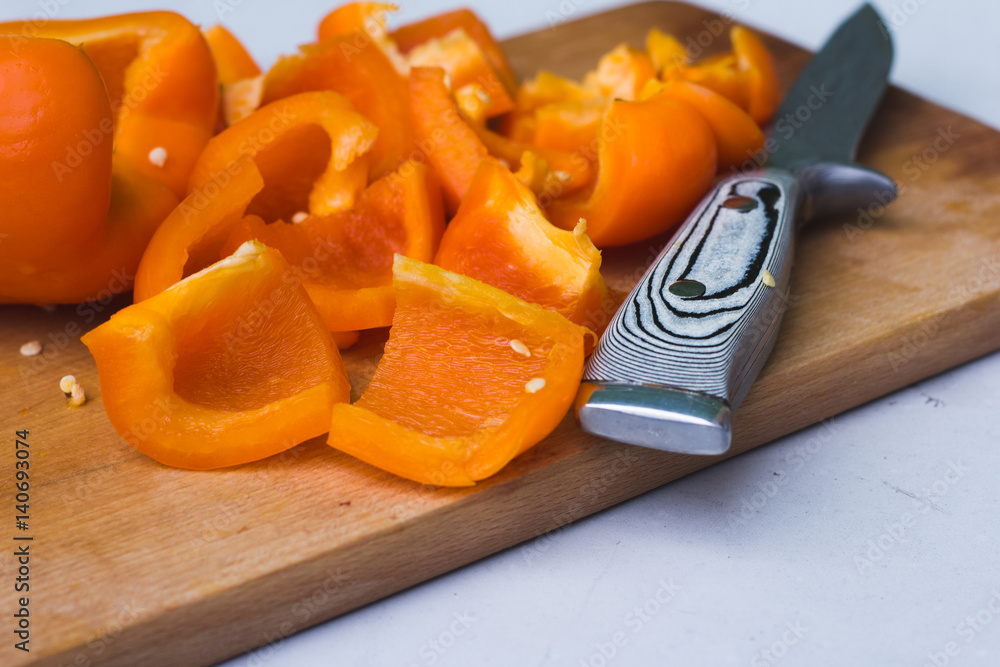 Orange pepper cut into pieces on wooden cutting board next to knife