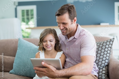 Smiling father and daughter sitting on sofa 