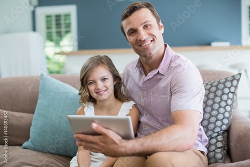 Father and daughter sitting on sofa using tablet
