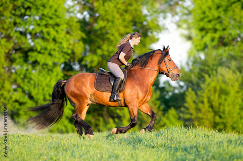 Horseback riding. Young woman is riding a horse in summertime. Girl with horse runs fast in field. Horse rider