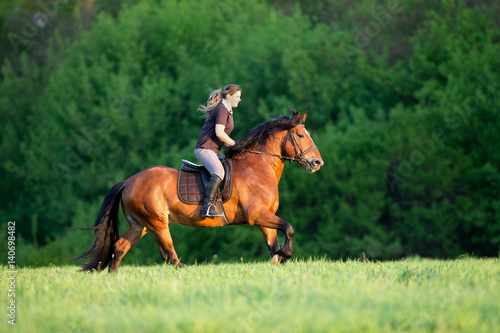 Horseback riding. Young woman is riding a horse in summertime. Girl with horse runs fast in field. Horse rider