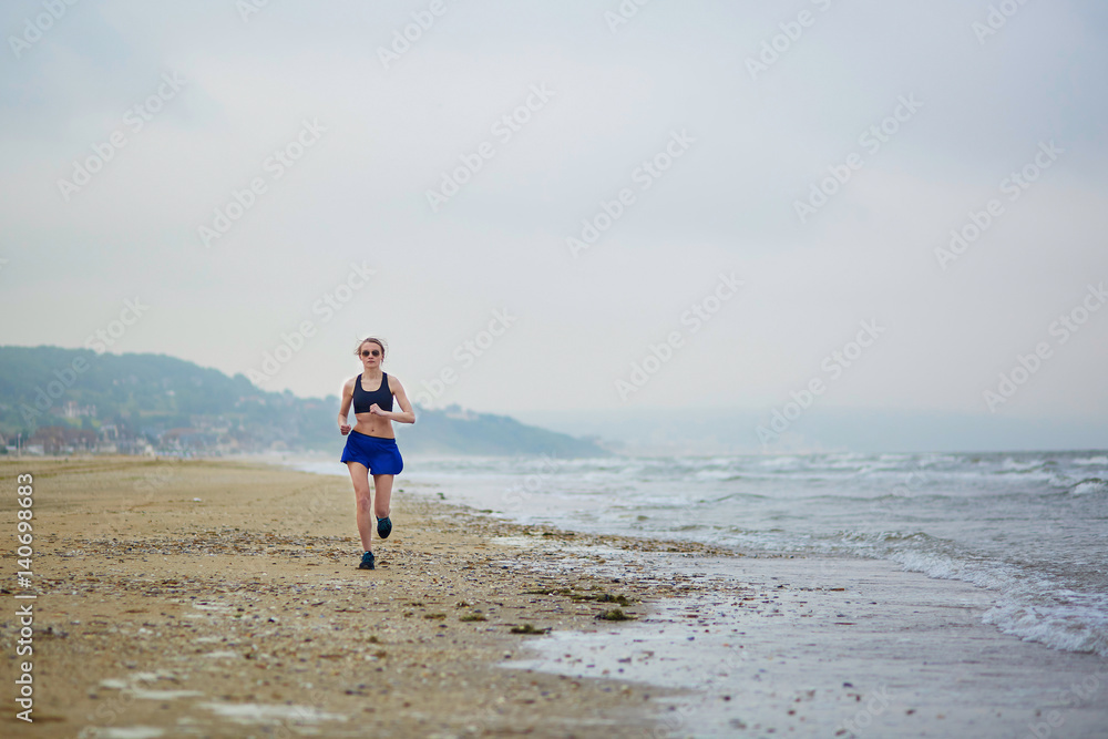 Young fitness running woman jogging on beach