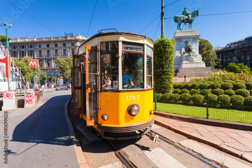 The old yellow tram has stopped on the tram stop near metro station Cairoli which located on the Piazzale Cairoli and the bronze monument to Giuseppe Garibaldi on Piazzale Cairoli. MILAN, ITALY
