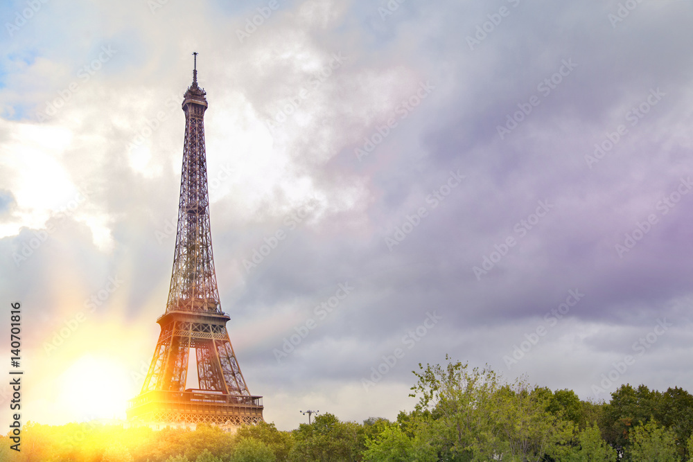 View on Eiffel tower over green summer trees with sunset rays. Beautiful Romantic background. Eiffel Tower from Champ de Mars, Paris, France.