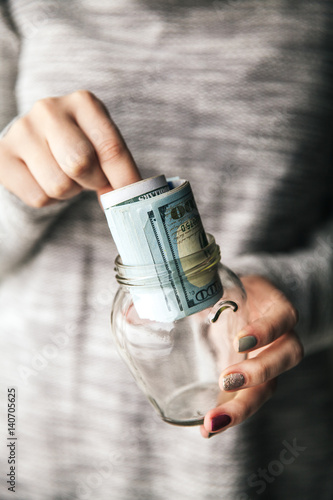 Money in glass jars in the women's hands with a nice manicure and modern sweater. Business offer.