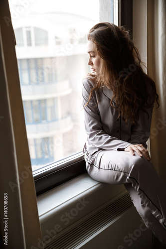 Vertical image of woman sitting on windowsill