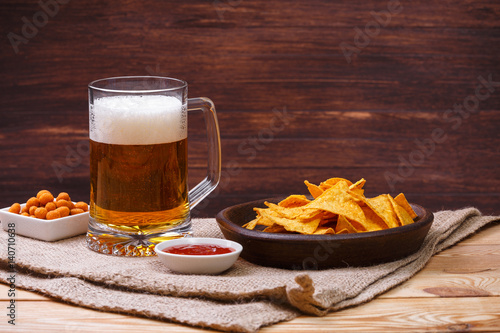 Glass of beer. Nachos chips. Tortilla snack. Mexican salsa nuts. Appetizer with sweet salsa or chilli sauce. Mug or pint of ale. On rustic wooden background.