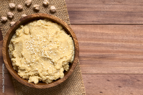 Hummus oder Kichererbsenaufstrich mit Sesam bestreut in Holzschüssel, fotografiert mit natürlichem Licht (Selektiver Fokus, Fokus auf den Aufstrich) photo