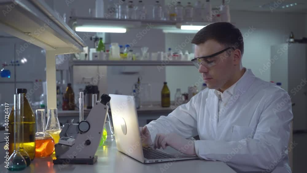 Lab technician entering data on laptop. Professional scientist working with computer in the medical or microbiological laboratory alone. adult focused man chemist engineer wearing in white coat. Lab technician entering data on laptop. Professional scientist working with computer in the medical or microbiological laboratory alone. adult focused man chemist engineer wearing in white coat.